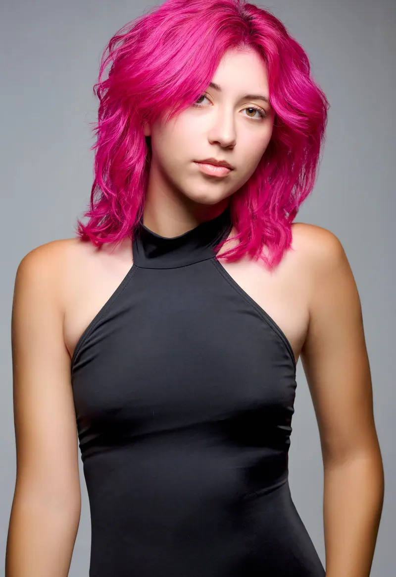 Fashion portrait featuring a model with vibrant pink hair and a black strapless dress in a studio setting.
