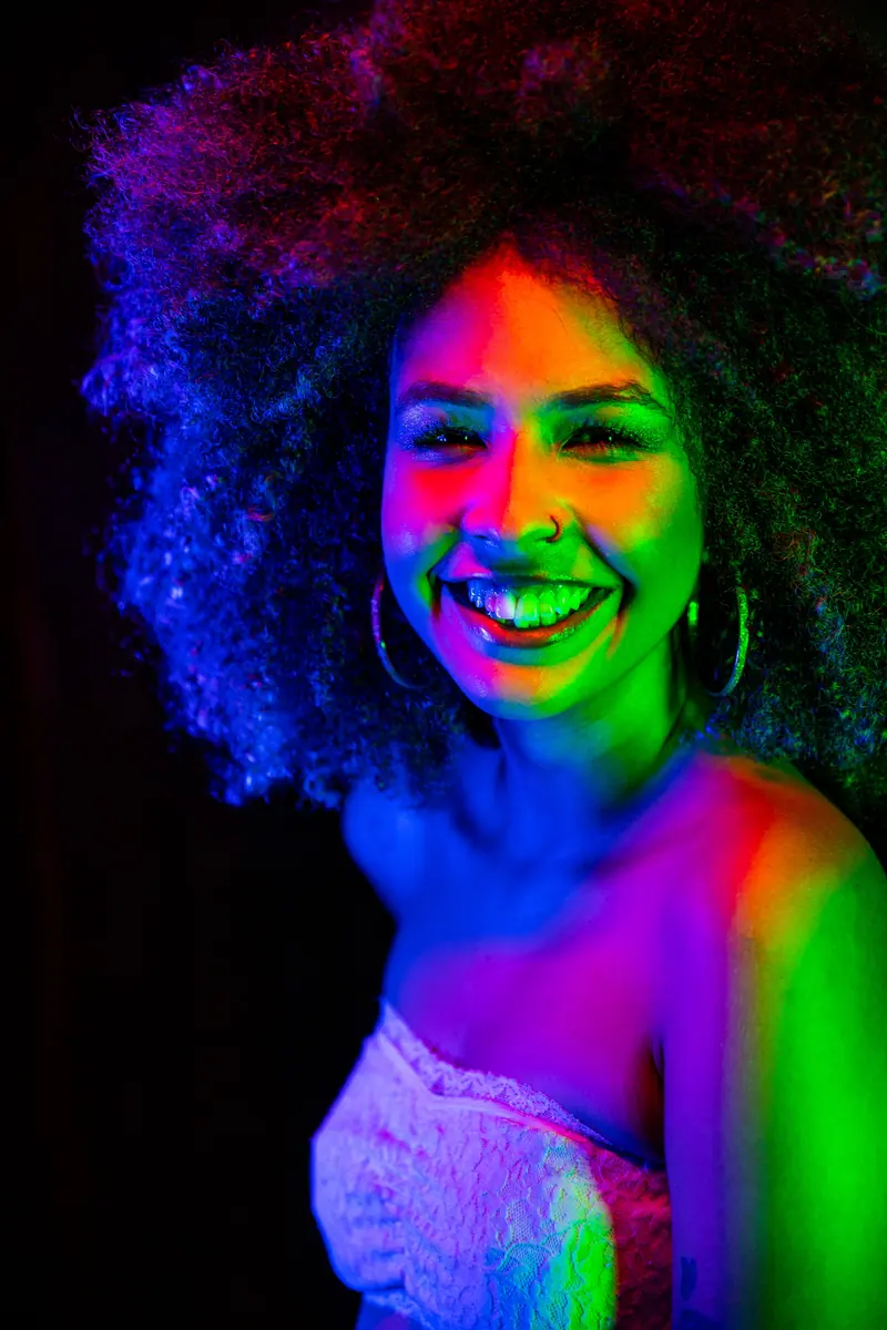 Laughing woman with a big natural afro lit in blue, green and magenta