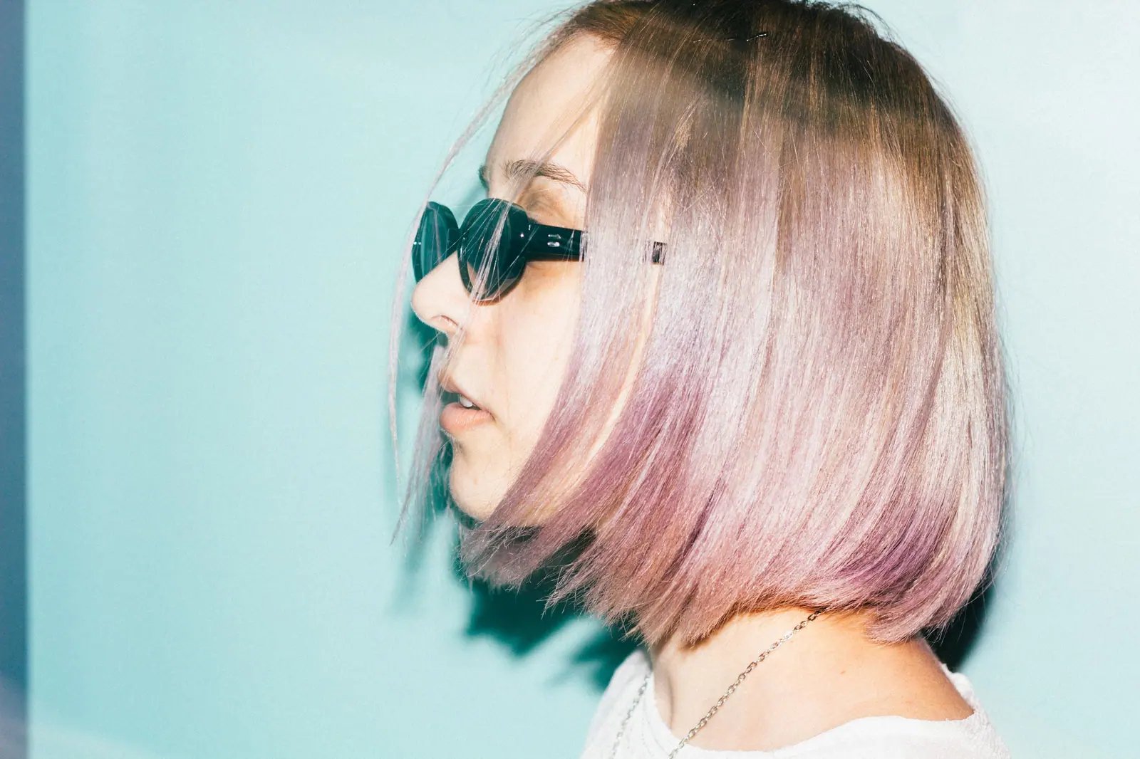 Side profile of a trendy woman with pink dyed hair wearing sunglasses in a studio shoot.