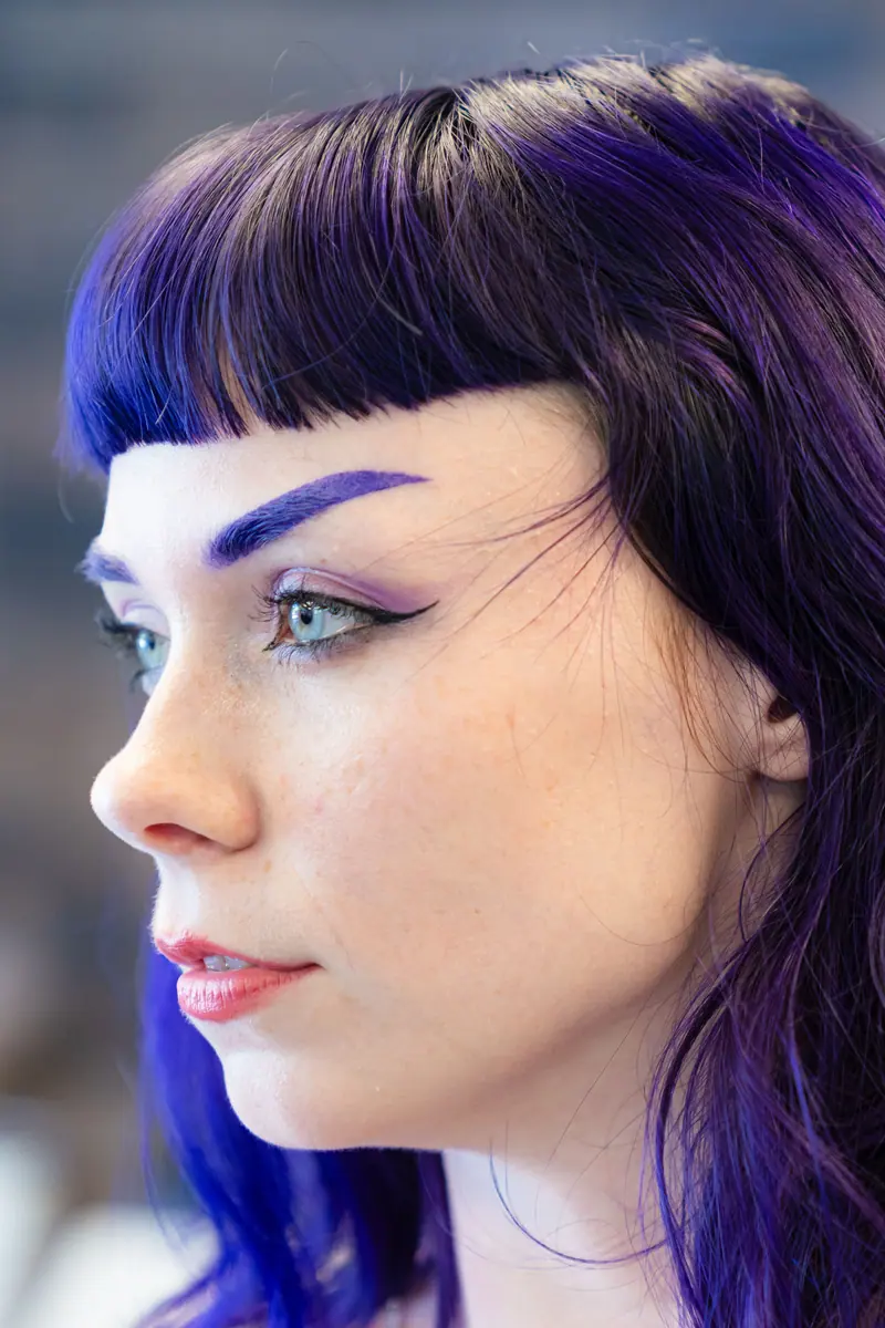 Close-up side profile of a young woman with striking purple hair and makeup