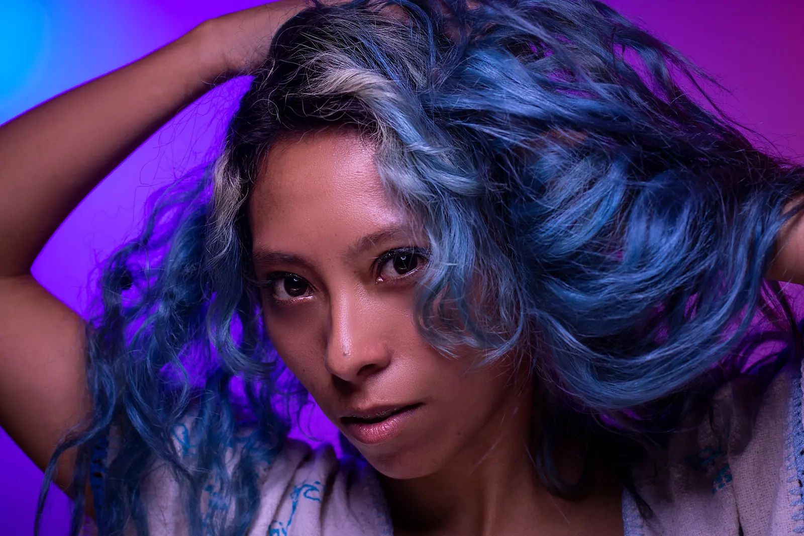 Model with blue-violet curls under purple light