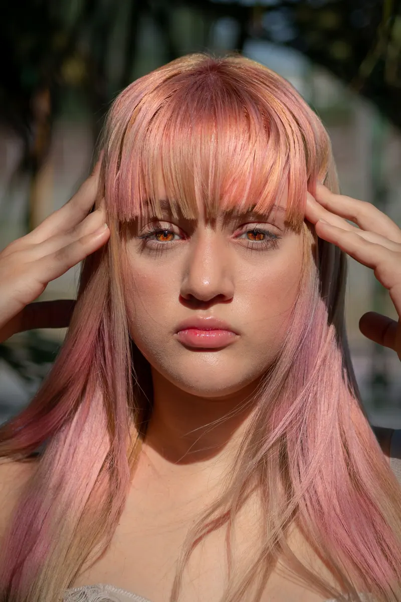 Close-up portrait of a young woman with pink hair in natural light outdoors.