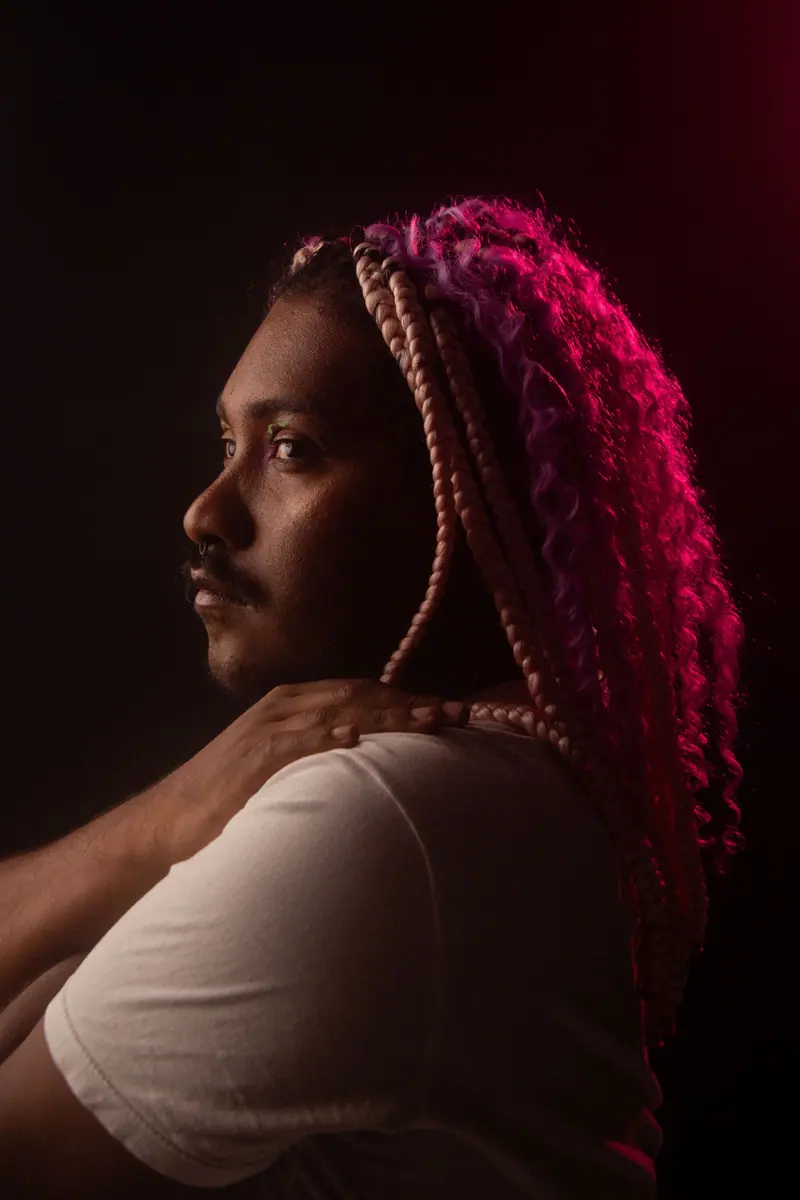 Side profile of an adult with colorful hair in dim lighting, showcasing creative style.