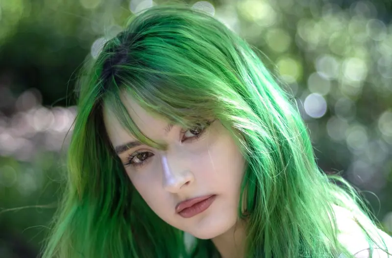 Close-up of a young woman with vibrant green hair in a natural setting.