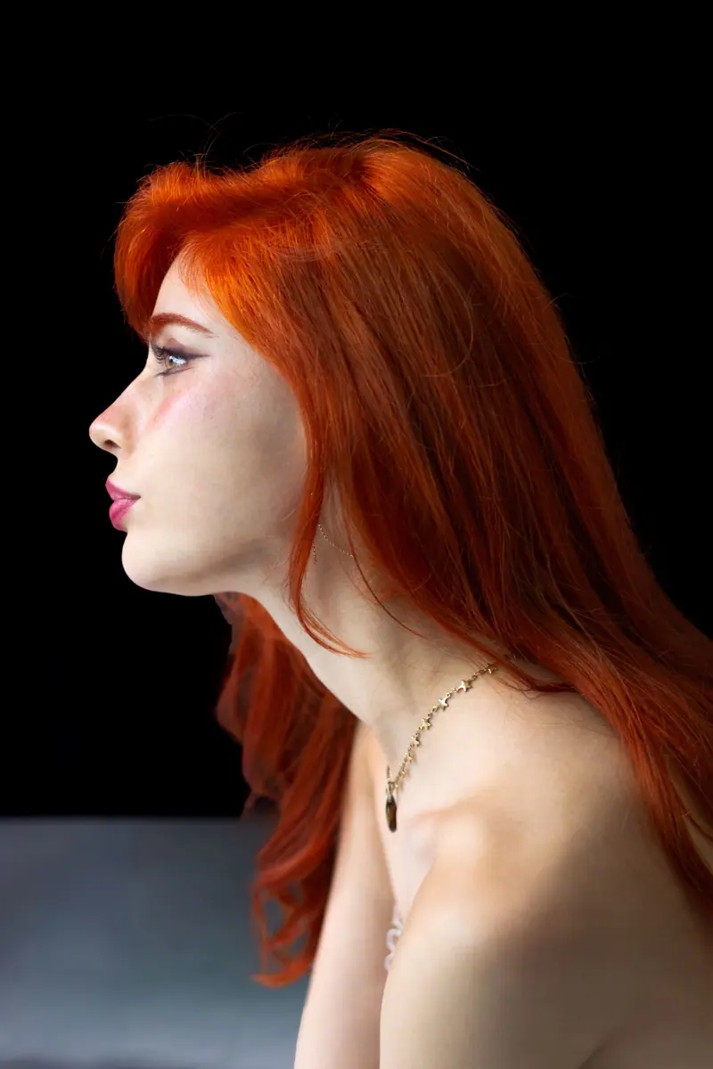 Profile of a woman with vivid copper hair against a black backdrop