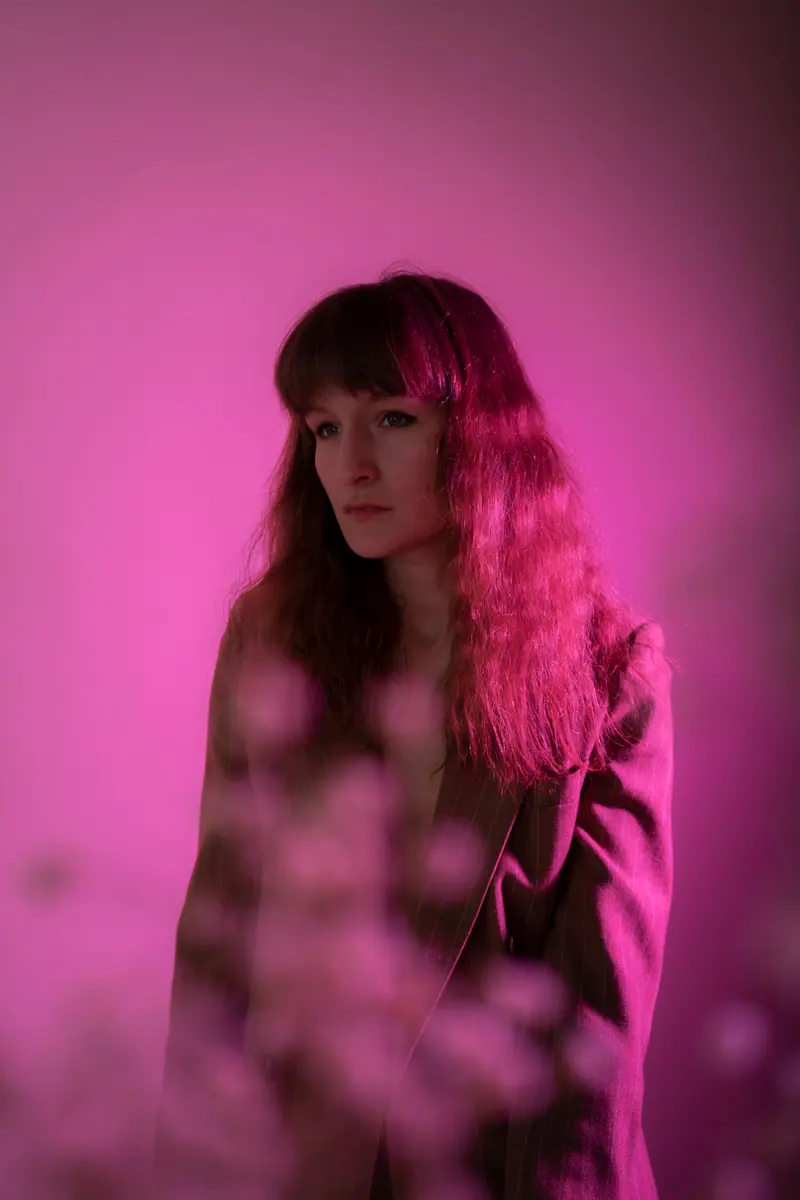 Artistic portrait of a woman with brown hair in moody pink lighting, creating a fashion-forward look.