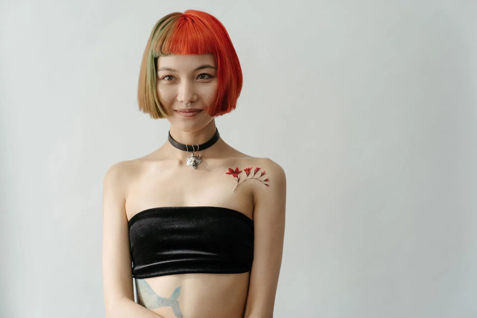 Woman with a sharp two-tone red and honey bob and a choker against a plain white wall