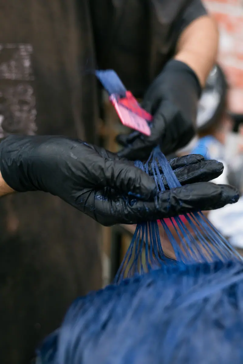 Colorist brushing bright blue dye through a client's sectioned hair