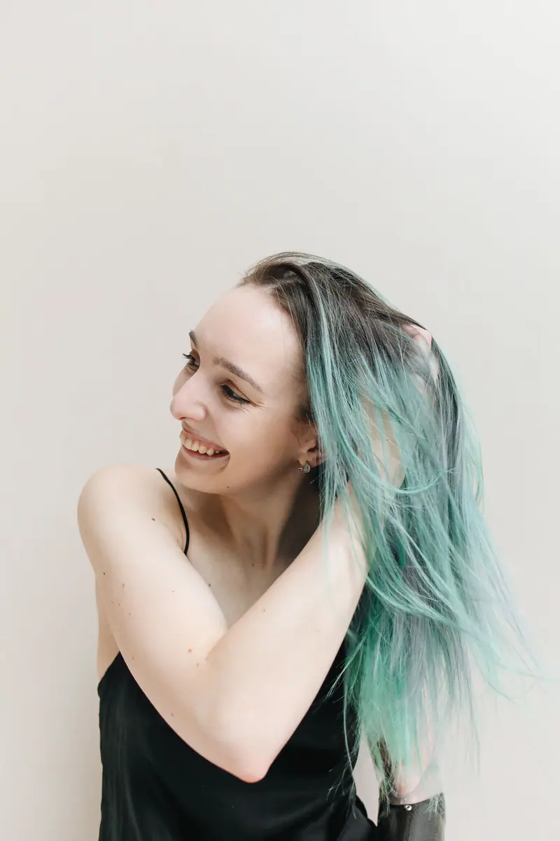 Smiling woman touching her pastel blue-green hair