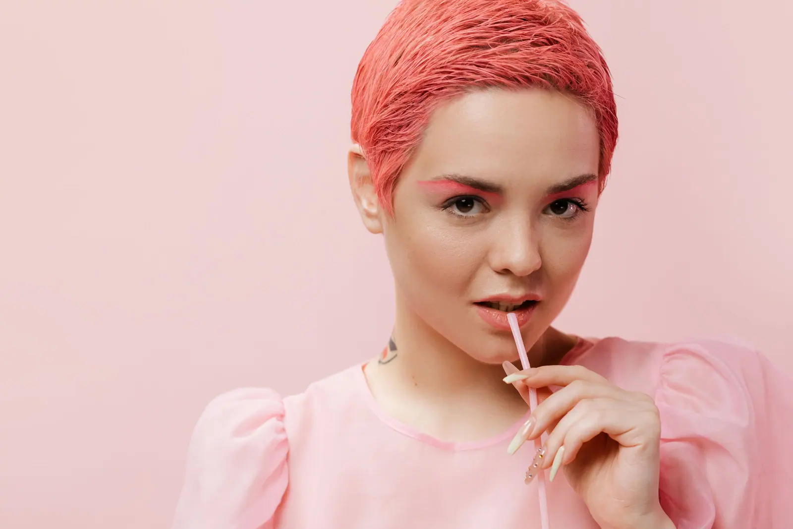 A trendy young woman with pink hair poses confidently in a studio setting, showcasing modern fashion.