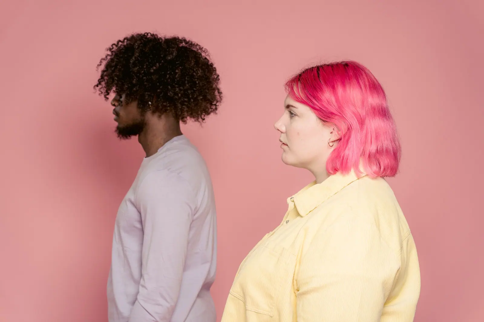 Side profile of diverse couple in a studio setting with pink background.