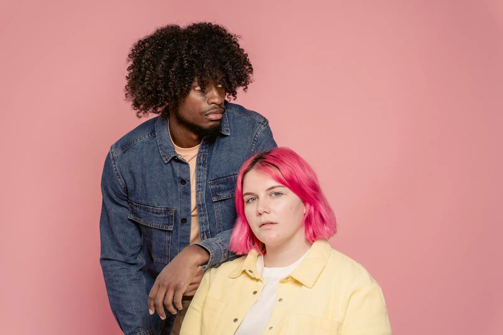 Two diverse individuals in a studio setting with pink background.