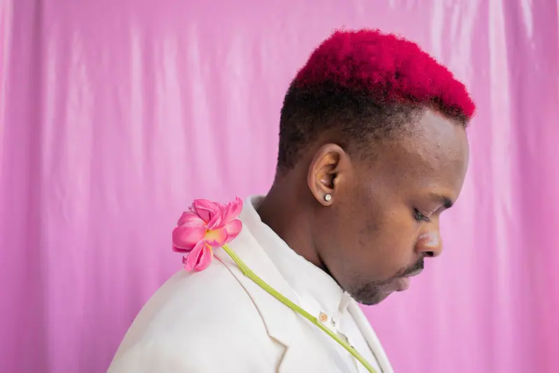 Man with vibrant pink hair and a flower against pink
