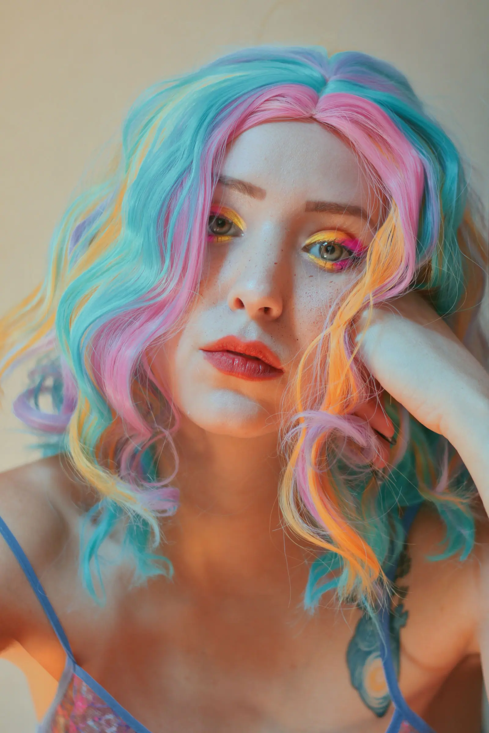 Woman with wavy pastel rainbow hair in pink, aqua, lilac and peach, resting her chin on her hand