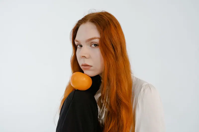 Long orange hair with a tangerine resting on a shoulder
