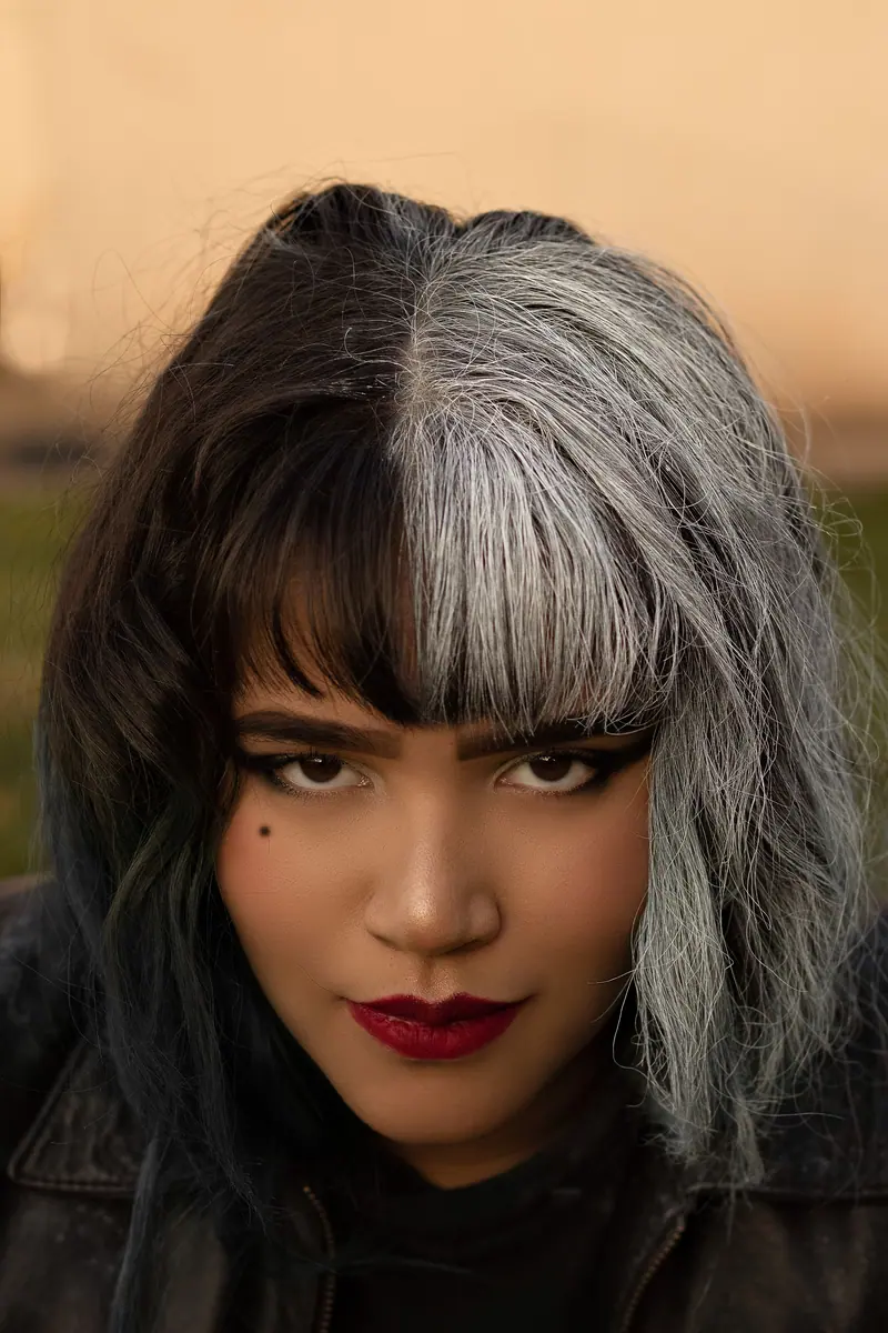 Close-up portrait of a woman with distinctive dual-toned hair and bold makeup.