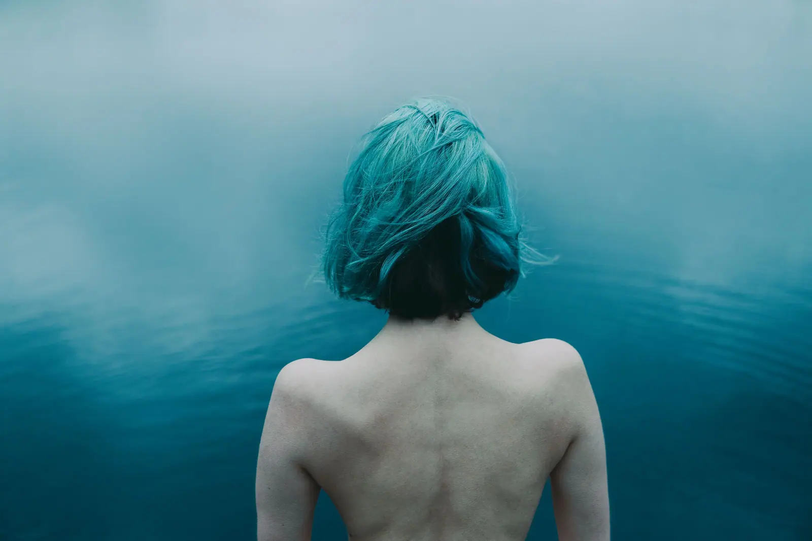 Woman with a sea-glass teal bob, seen from behind, standing in misty blue water